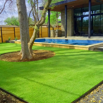 Section of a yard with artificial turf around a pool and a large tree shading the space. A modern covered porch attached to the house is behind the pool.