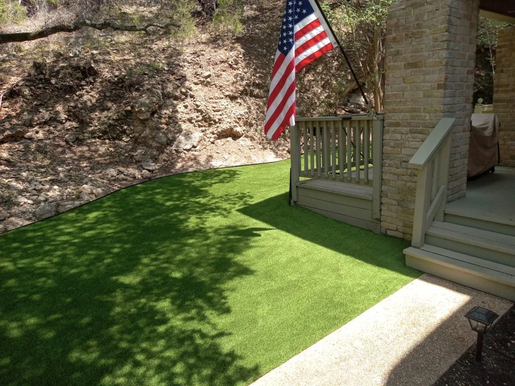 Artificial turf installation beside a rocky Texas Hill Country slope and brick home with deck — How Much Does Artificial Turf Cost in Lakeway 2026 Guide by Lone Star Turf