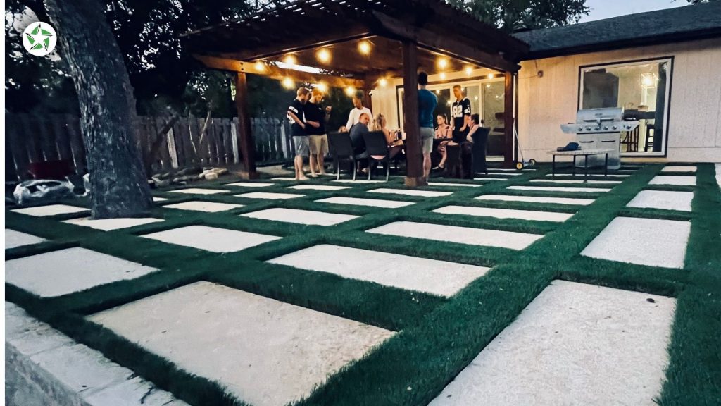 Friends gathered under a lit pergola beside a turf and paver patio on a Saturday evening in year one with artificial turf, Year One With Artificial Turf: What to Expect, Lone Star Turf Texas