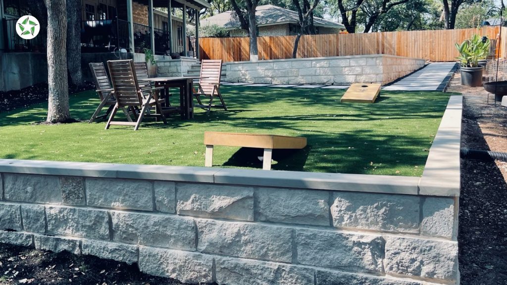 Settled turf lawn framed by a limestone retaining wall and mature oaks at the twelve-month mark of year one with artificial turf, Year One With Artificial Turf: What to Expect, Lone Star Turf Texas