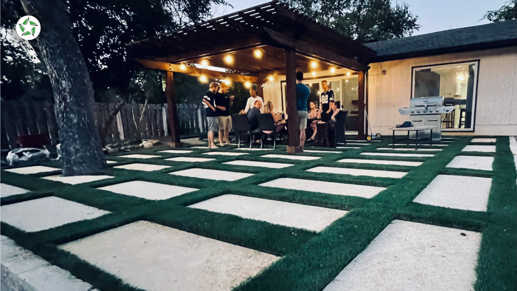 Guests gathered on a paver and turf patio with a grill set back from the grass, showing how to maintain artificial turf around heat sources, How to Clean and Maintain Artificial Turf (Without Wrecking It), Lone Star Turf Texas
