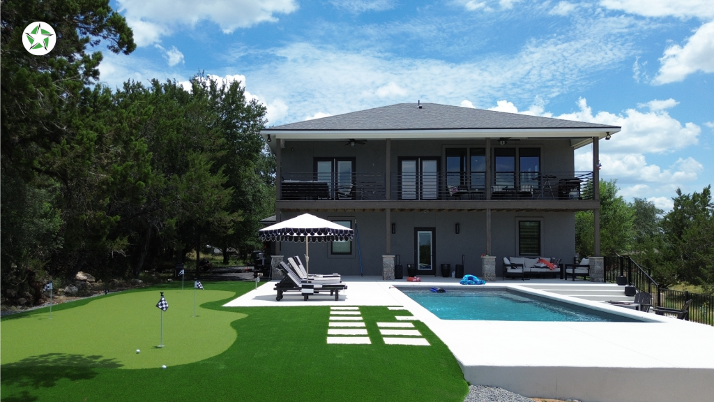 Backyard pool with concrete decking and a turf putting green, Lone Star Turf Texas, from Turf Around the Pool: Pavers vs. Concrete vs. Turf.