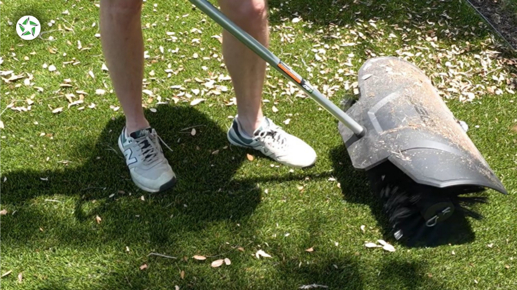 Homeowner sweeping fallen leaves off a turf lawn with a brush attachment to maintain artificial turf, How to Clean and Maintain Artificial Turf (Without Wrecking It), Lone Star Turf Texas