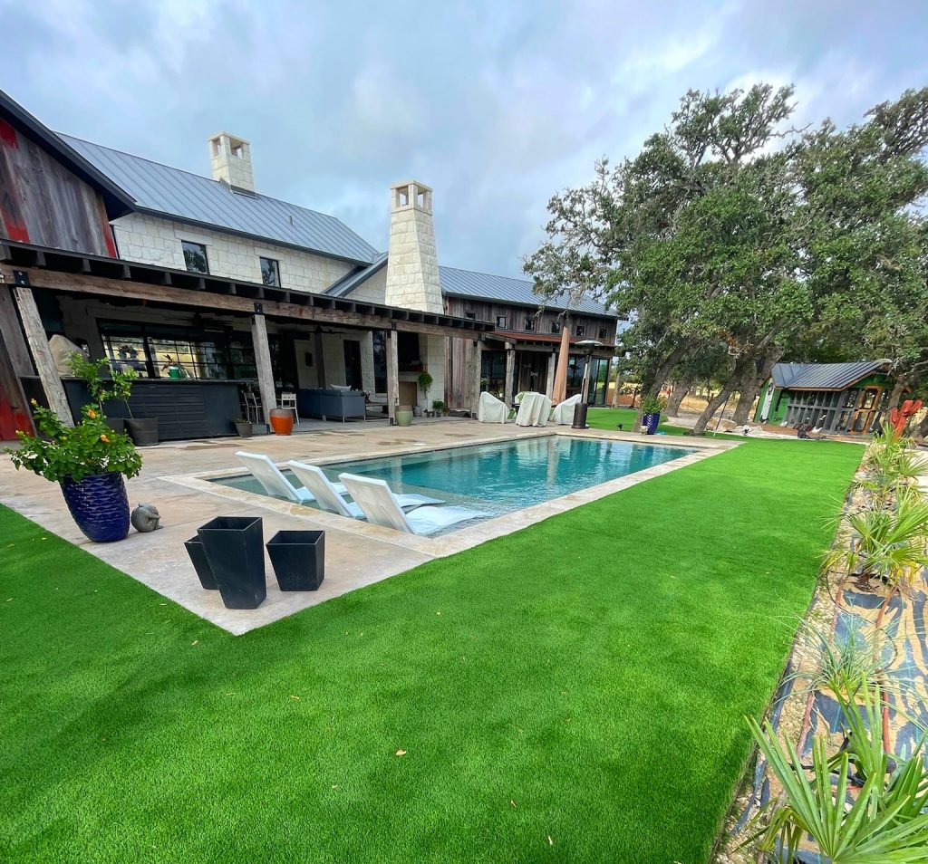 A low maintenance yard with turf installed around a pool decorated with potted plants and lounge chairs