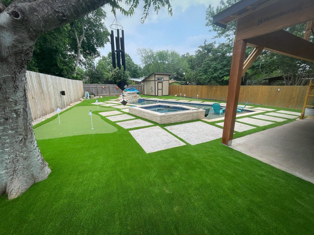 A residential backyard with professional turf installation in Texas, featuring a putting green, swimming pool, hot tub, and artificial turf lawn