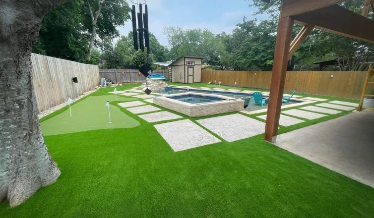 A residential backyard with professional turf installation in Texas, featuring a putting green, swimming pool, hot tub, and artificial turf lawn