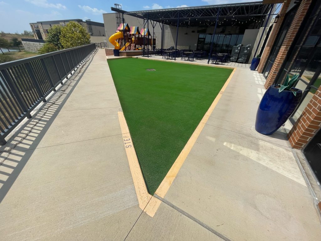 Triangular patch of artificial grass installed next to a restaurant outdoor seating area