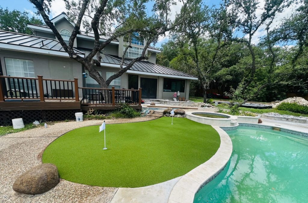 Low maintenance landscaping using artificial turf for a backyard putting green next to a pool.