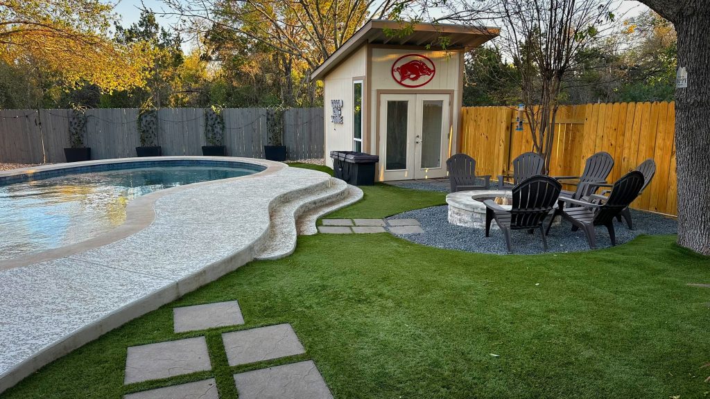 Low maintenance yard with artificial turf around a pool, fire pit, and shed.