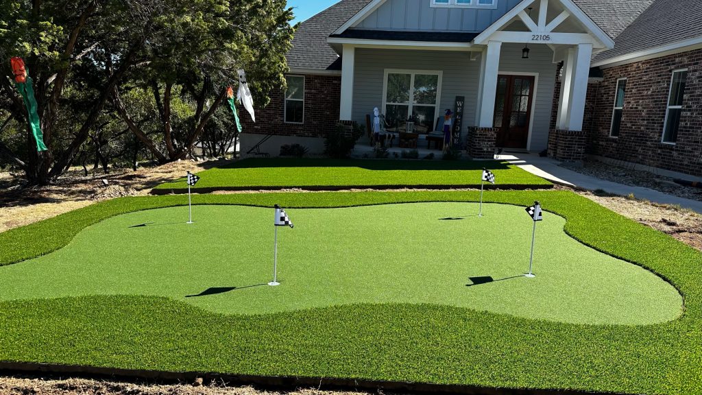 Putting green artificial turf in a residential yard with 4 holes and a small black and white flag at each one.