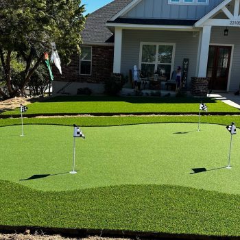 Putting green artificial turf in a residential yard with 4 holes and a small black and white flag at each one.