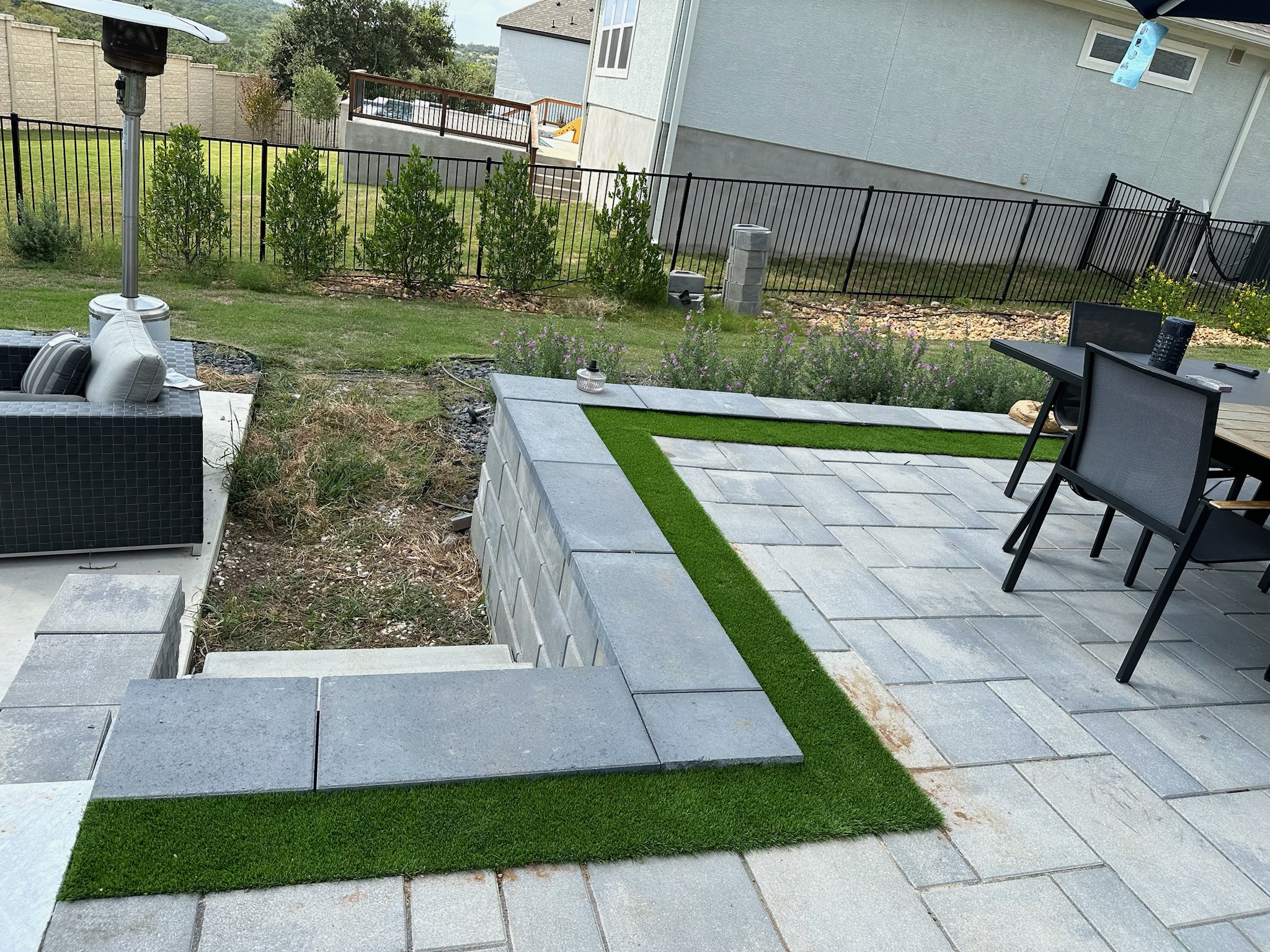 Stone pavers installed on a backyard deck with outdoor patio furniture and stairs down to a grassy area.