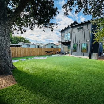 A large tree in a backyard with artificial turf and pavers installed.