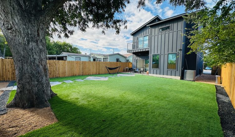 A large tree in a backyard with artificial turf and pavers installed.
