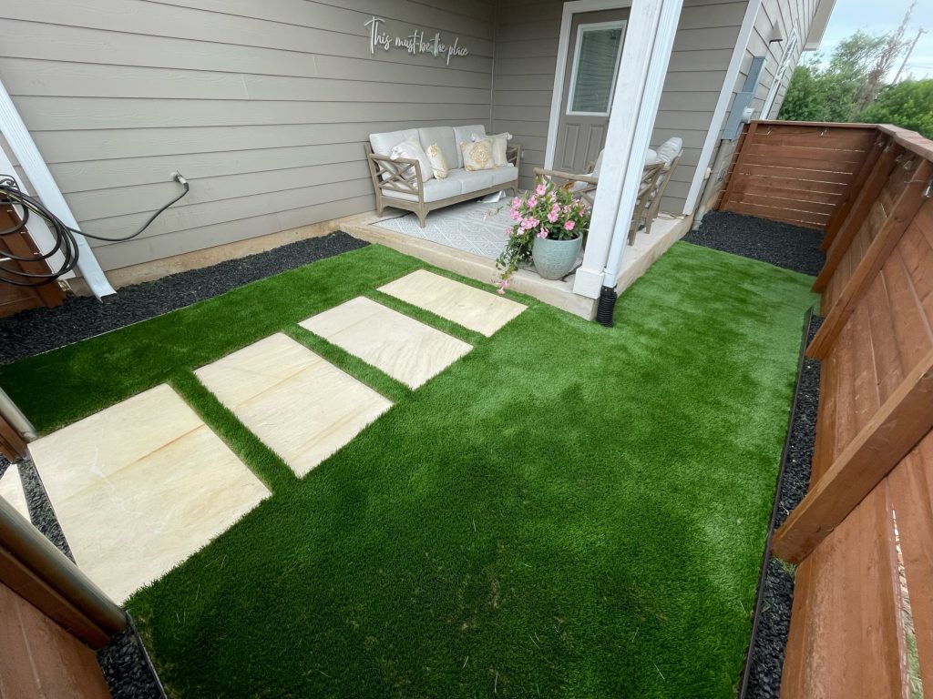 Small side yard with artificial turf and light colored square pavers leading from the gate to a cozy porch.