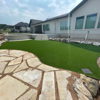 Artificial turf installation in backyard with stone feature and above ground pool.