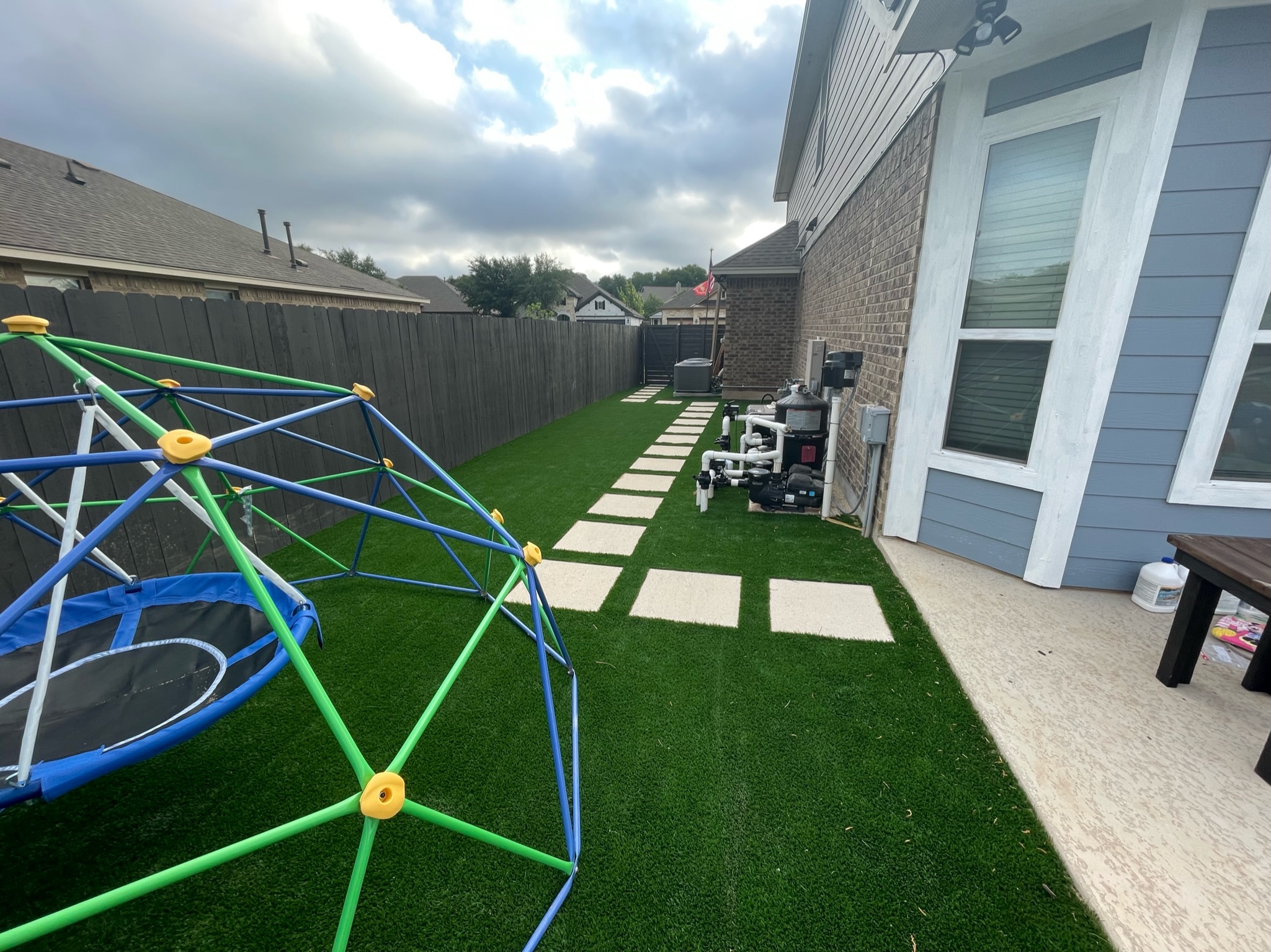 Residential Side Yard Turf and Pavers with Jungle Gym A kid's jungle gym and other toys on artificial turf installed along the side yard of a home with pavers leading to the door.