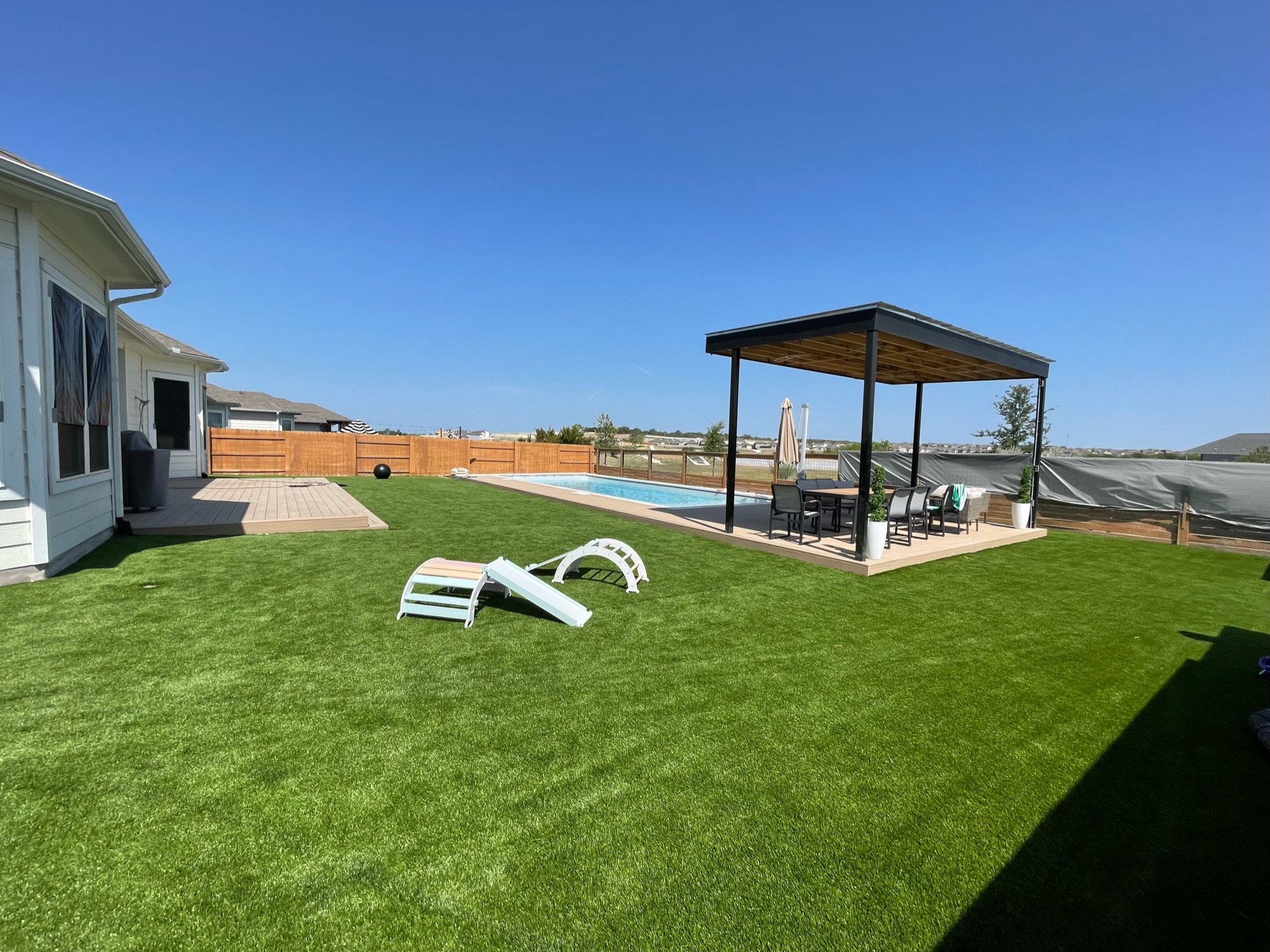 Residential Backyard Turf Install with Pool and Pergola Turf installed in a large backyard with a pool area, shaded pergola, and a small dog agility course.