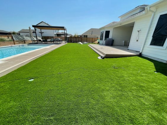 Turf installed between the back deck of a house and the pool area, with a pergola in the distance behind the pool. Artificial turf austin