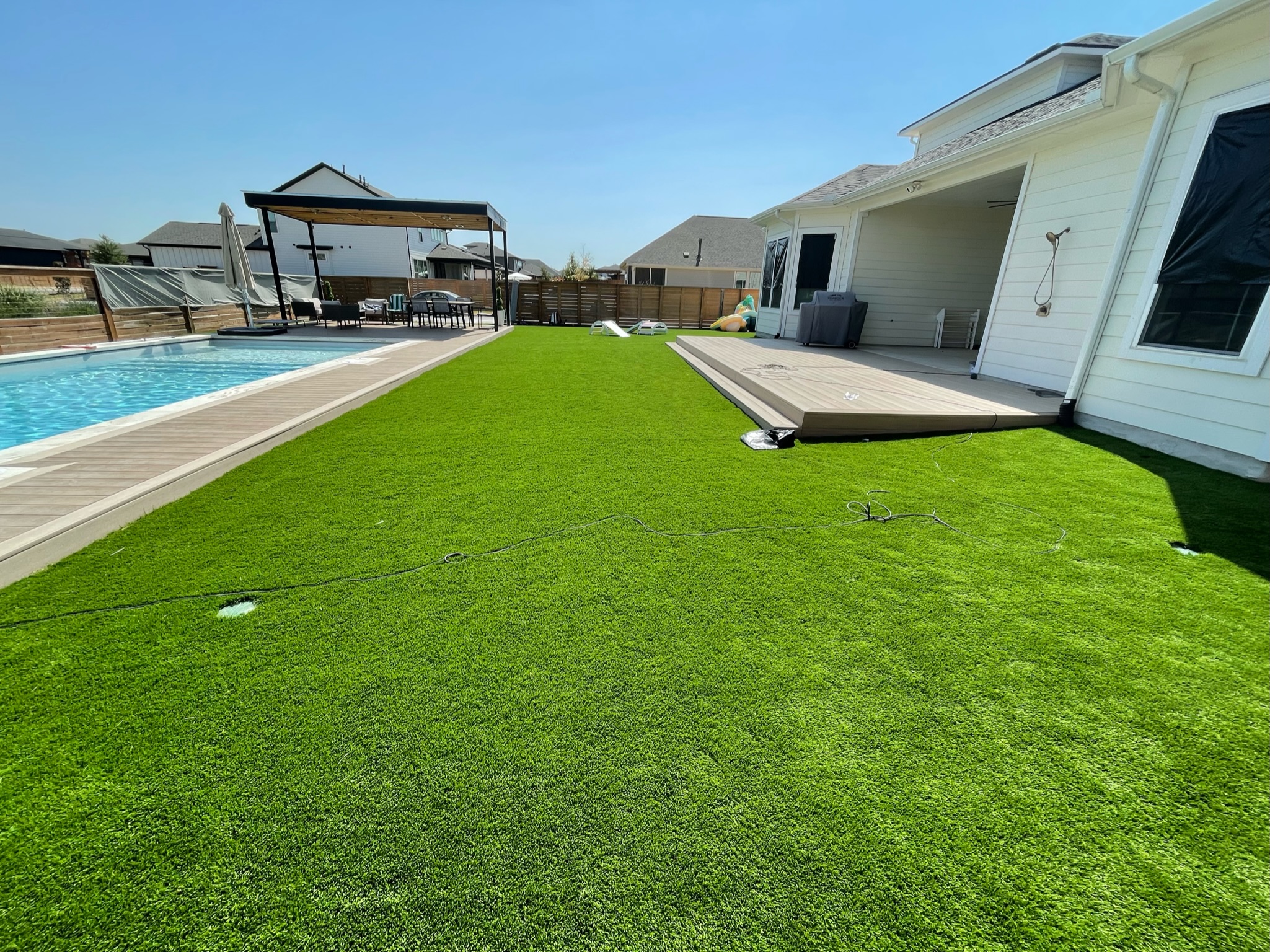 Residential Backyard Pool Pergola Turf Turf installed between the back deck of a house and the pool area, with a pergola in the distance behind the pool.