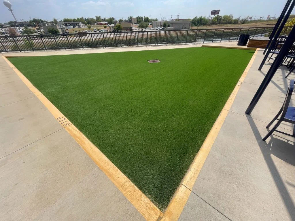 A completed commercial turf installation in Texas, depicting a large downward sloped rectangular area of turf, outlined by a stripe of yellow paint to warn of the slope.