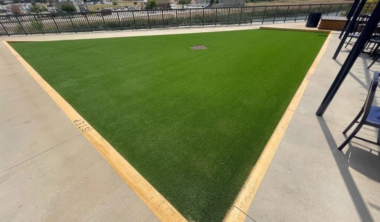 A completed commercial turf installation in Texas, depicting a large downward sloped rectangular area of turf, outlined by a stripe of yellow paint to warn of the slope.