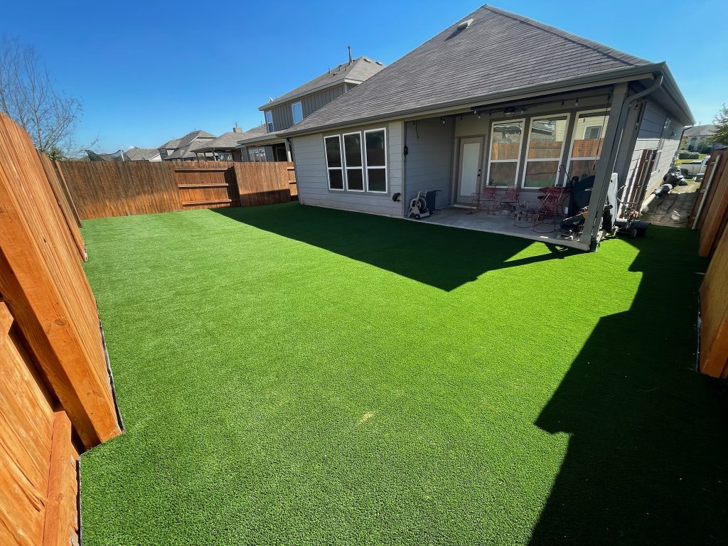 Low maintenance yard with artificial turf in the back of a small house with a porch.