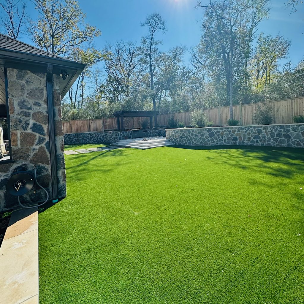Yard with artificial turf surrounded by a stone wall and a shaded pergola.