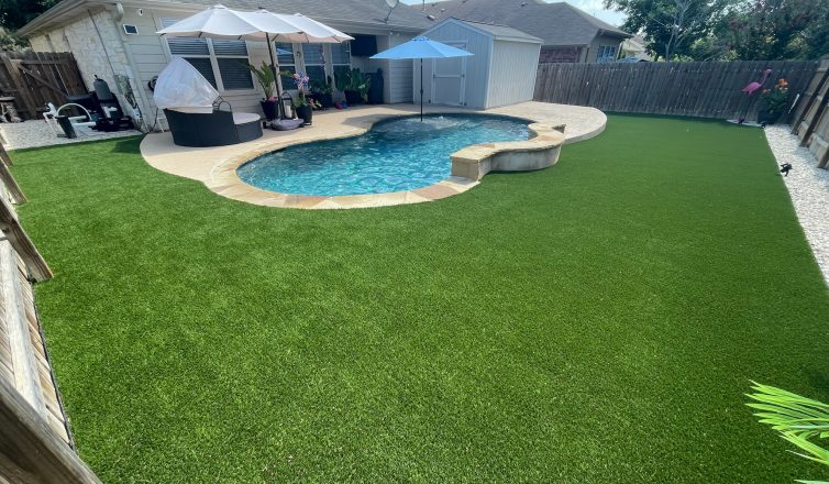 Artificial turf in a large backyard with an oval swimming pool near the house in the background.