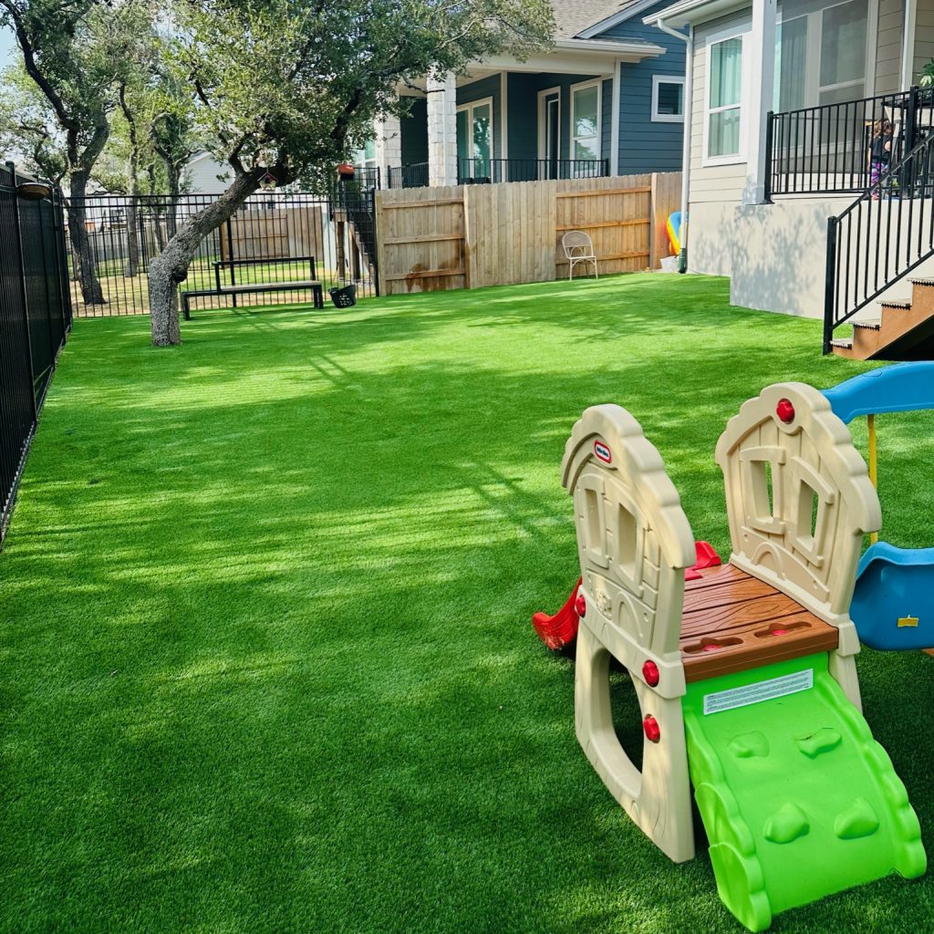 Backyard with a plastic kids' play set showing artificial turf safety