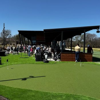crowds gathered at a putting green and golf range with artificial turf installed