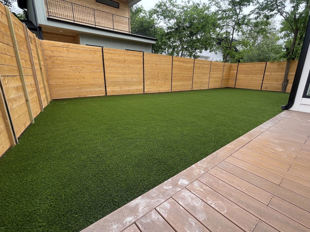 Low maintenance yard with tall wooden fencing surrounding it and part of a dark wood porch visible where the photographer is standing.