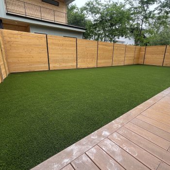 Low maintenance yard with tall wooden fencing surrounding it and part of a dark wood porch visible where the photographer is standing.