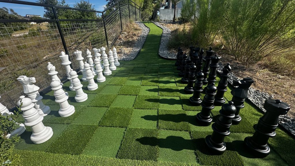 A giant chess board made out of two shades of artificial turf complete with 3 foot high chess pieces.