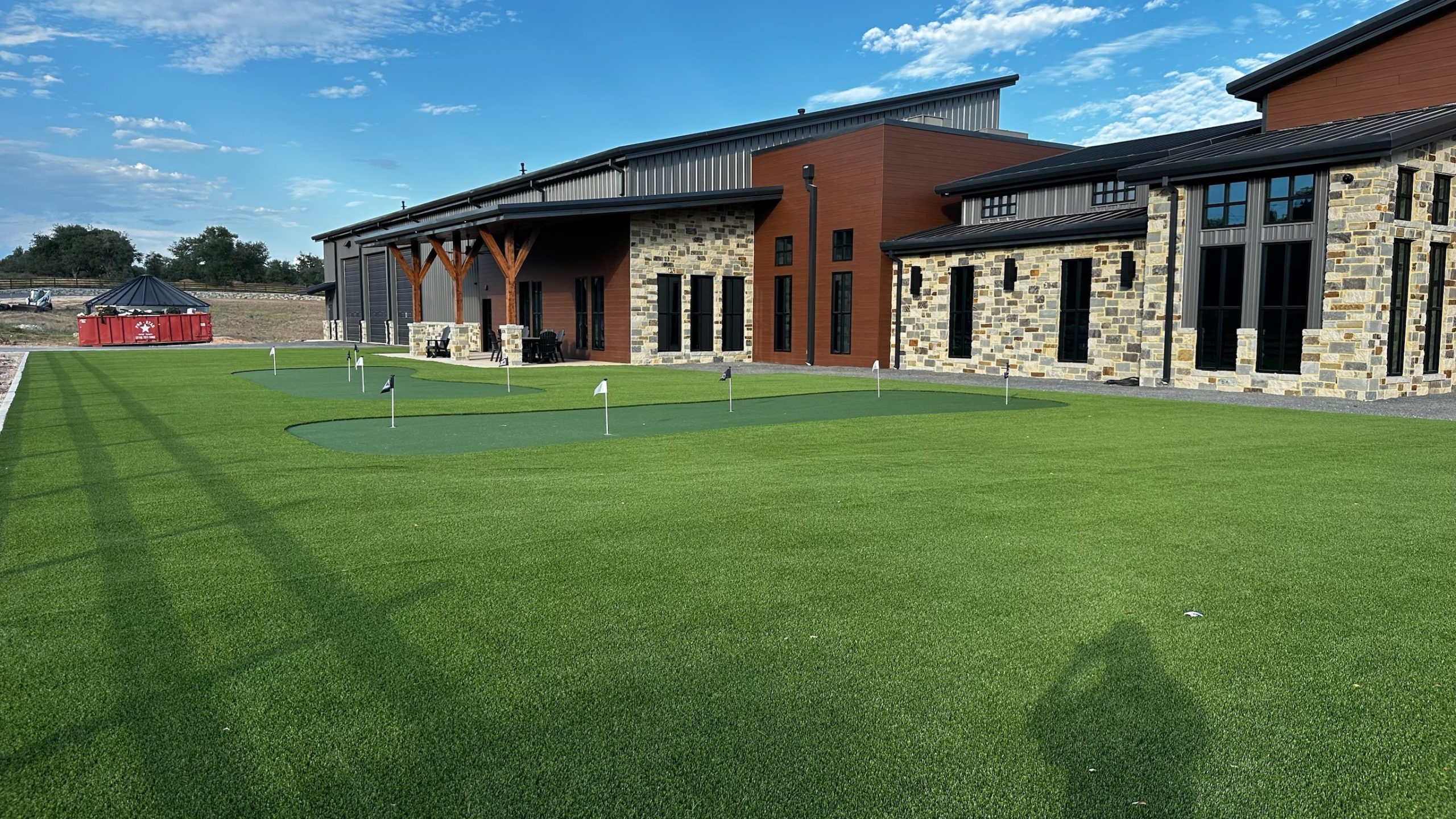 Photo of the back area of Nickel Rock with artificial turf installed including two putting greens for staff and client use.