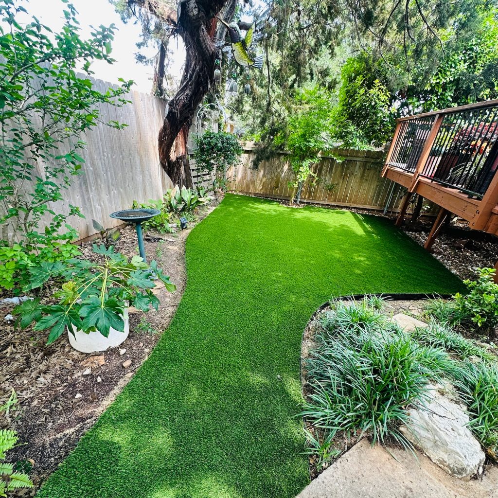 Yard with artificial turf that prevents weeds, even with a garden and natural plans surrounding it.