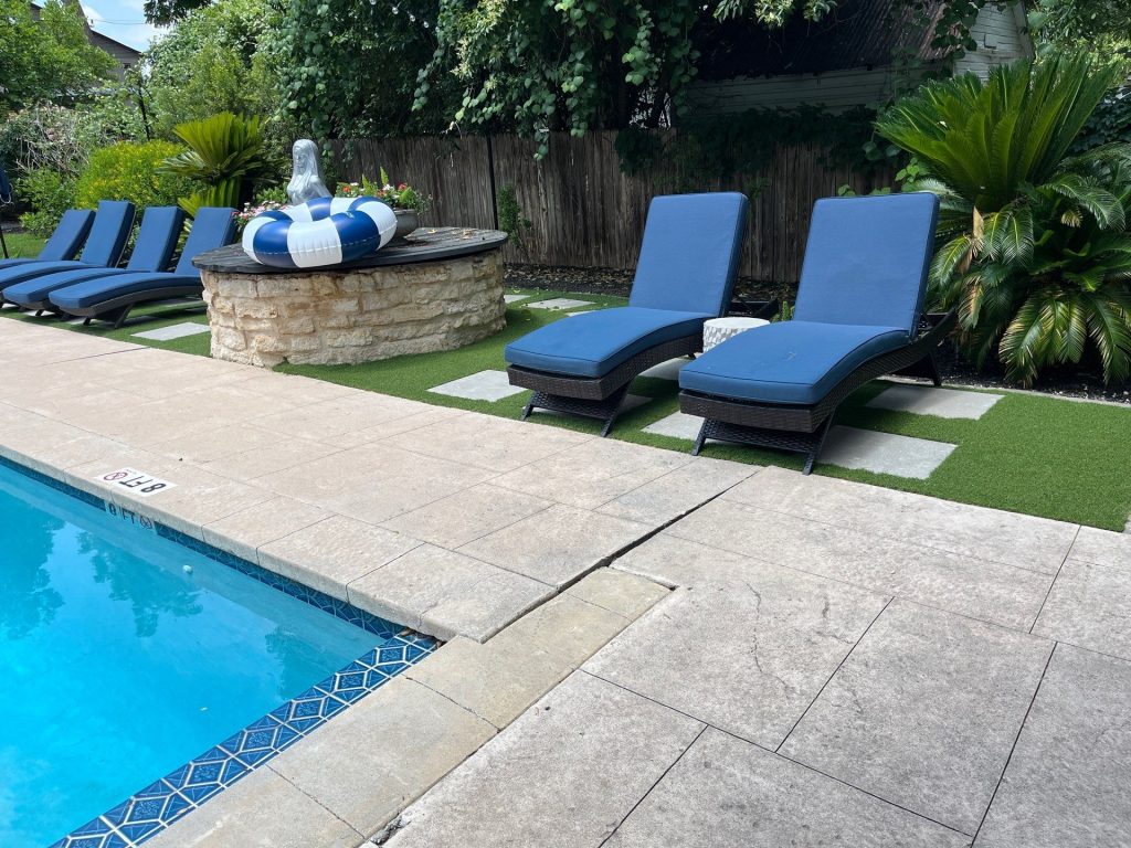 Artificial turf installed around a Texas pool patio with blue lounge chairs and tropical landscaping answering Why Won't Grass Grow in My Texas Backyard — Lone Star Turf poolside solution