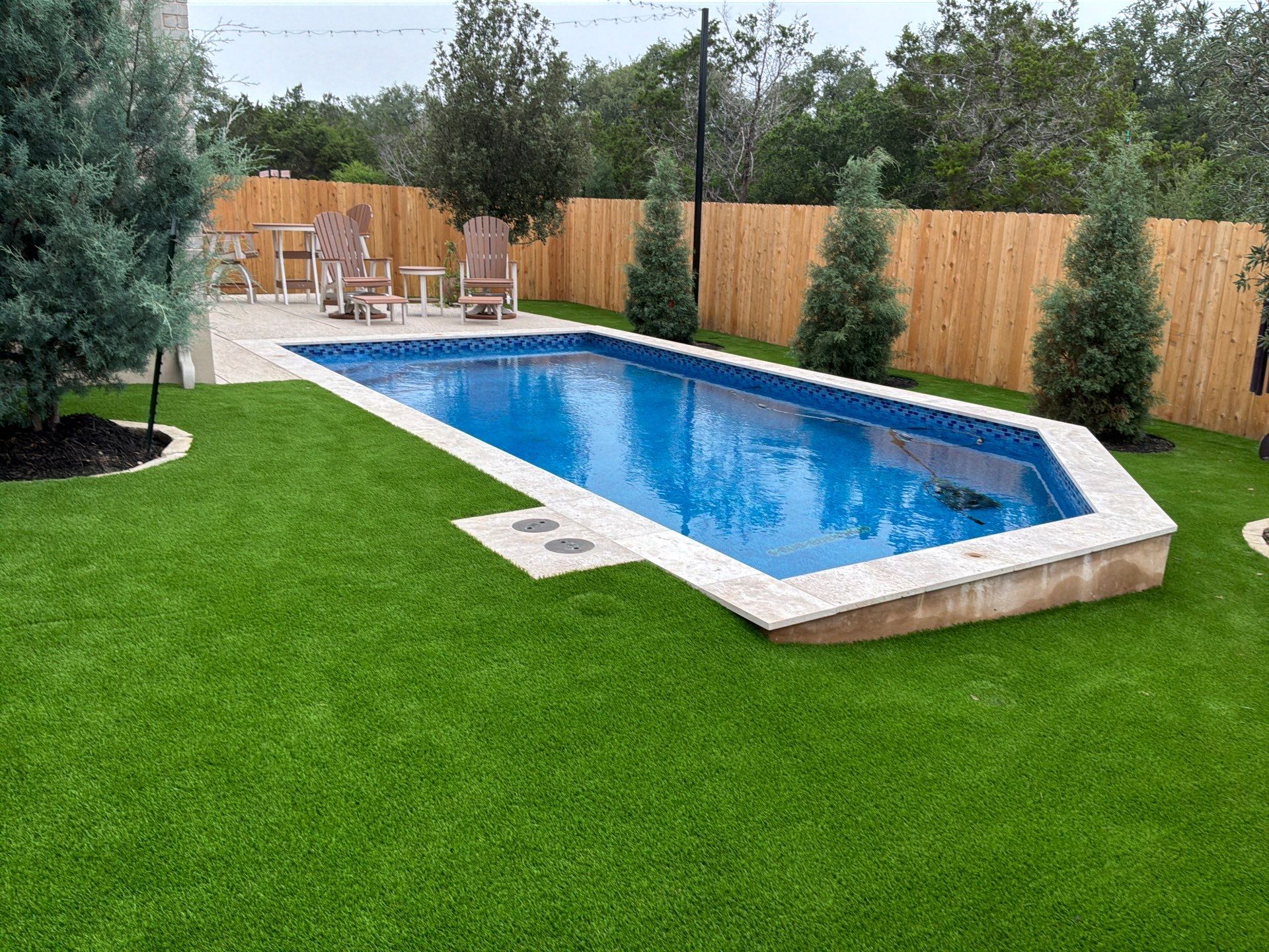 Backyard swimming pool surrounded by artificial turf and a wood privacy fence