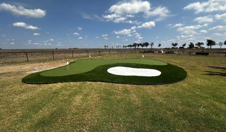 Putting green with three different types of artificial turf in the middle of a larger natural grass field.
