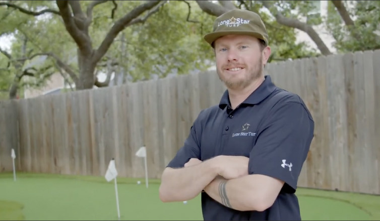 Lone Star Turf founder Patrick Walthall posing with his arms folded, smiling. He is wearing a branded Lone Star Turf polo shit and hat.
