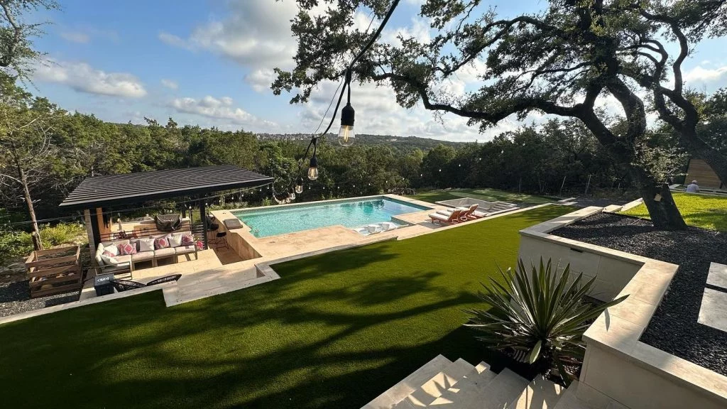 A view of a backyard with new artificial turf installed, looking down on the lawn area and a pool from the main house slightly up a hill.