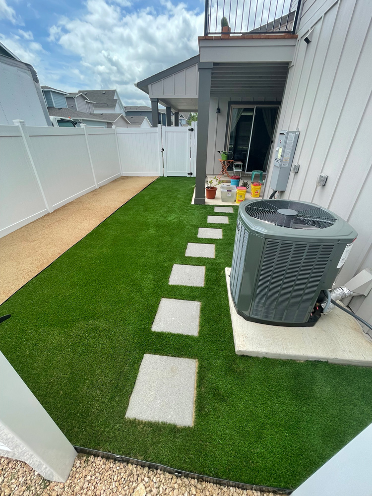 Artificial turf installed along the side of a house with square pavers creating a path to the covered porch.