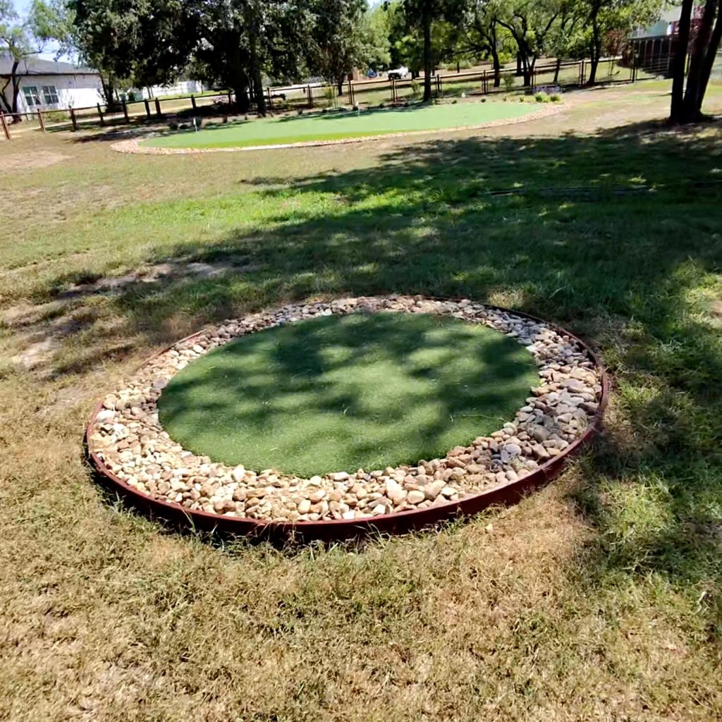 A small circular chipping mat for backyard golf with a stone gravel border.