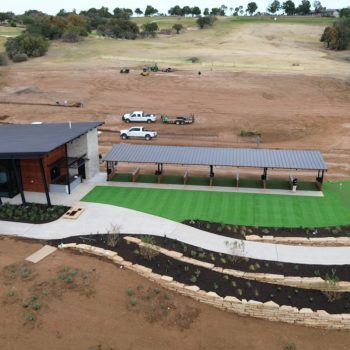Overhead photo from a drone of a fresh artificial turf installation with a putting green, creating a bright pop of green in the middle of a large area of undeveloped dirt.
